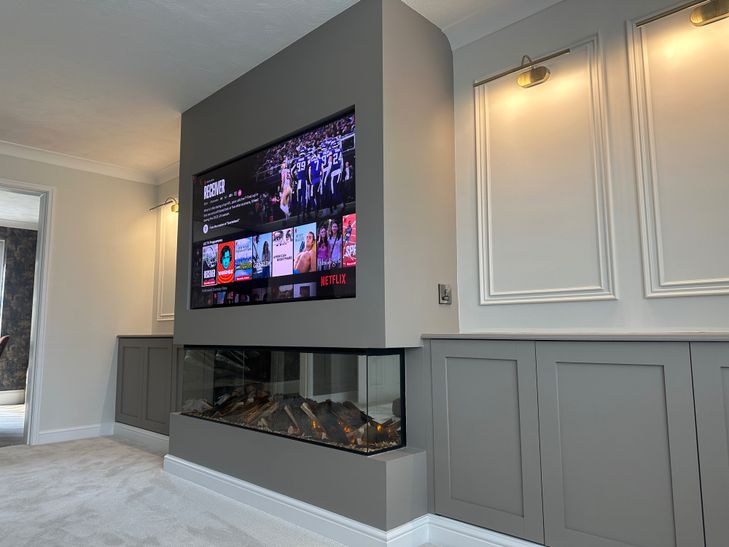 Bespoke sage-green media wall with built-in alcoves and electric fireplace by Dyson Joinery